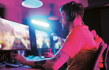 Foto von mehreren Gamern, die nebeneinander an unterschiedlichen Rechner zocken. Das Licht ist rötlich-dunkel.