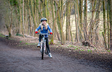Foto eines Mädchens im Grundschulalter, das auf einem Waldweg im Winter aufs Rad aufsteigt.