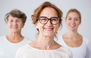 Symbolbild von drei Frauen unterschiedlichen Alters, die in weißen T-Shirts fröhlich in die Kamera blicken