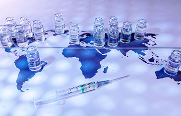 Symbolbild von Impfdosen, die auf einer blauen Weltkarte verteilt stehen. Daneben liegt eine Spritze mit einer Impfdosis.