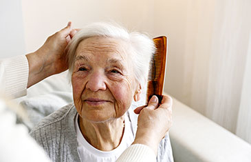 Foto einer alten Dame, der jemand die Haare kämmt