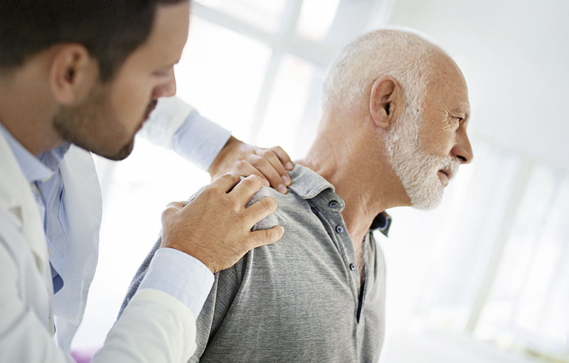 Foto eines Arztes mittleren Alters, der die Schulter eines älteren Mannes untersucht