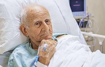 Foto eines alten Mannes mit Zugang in seiner linken Hand, der traurig in einem Intensivbett liegt