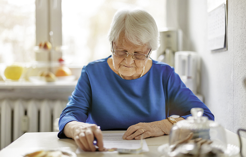Foto einer älteren Frau, die an einem Küchentisch Dokumente liest